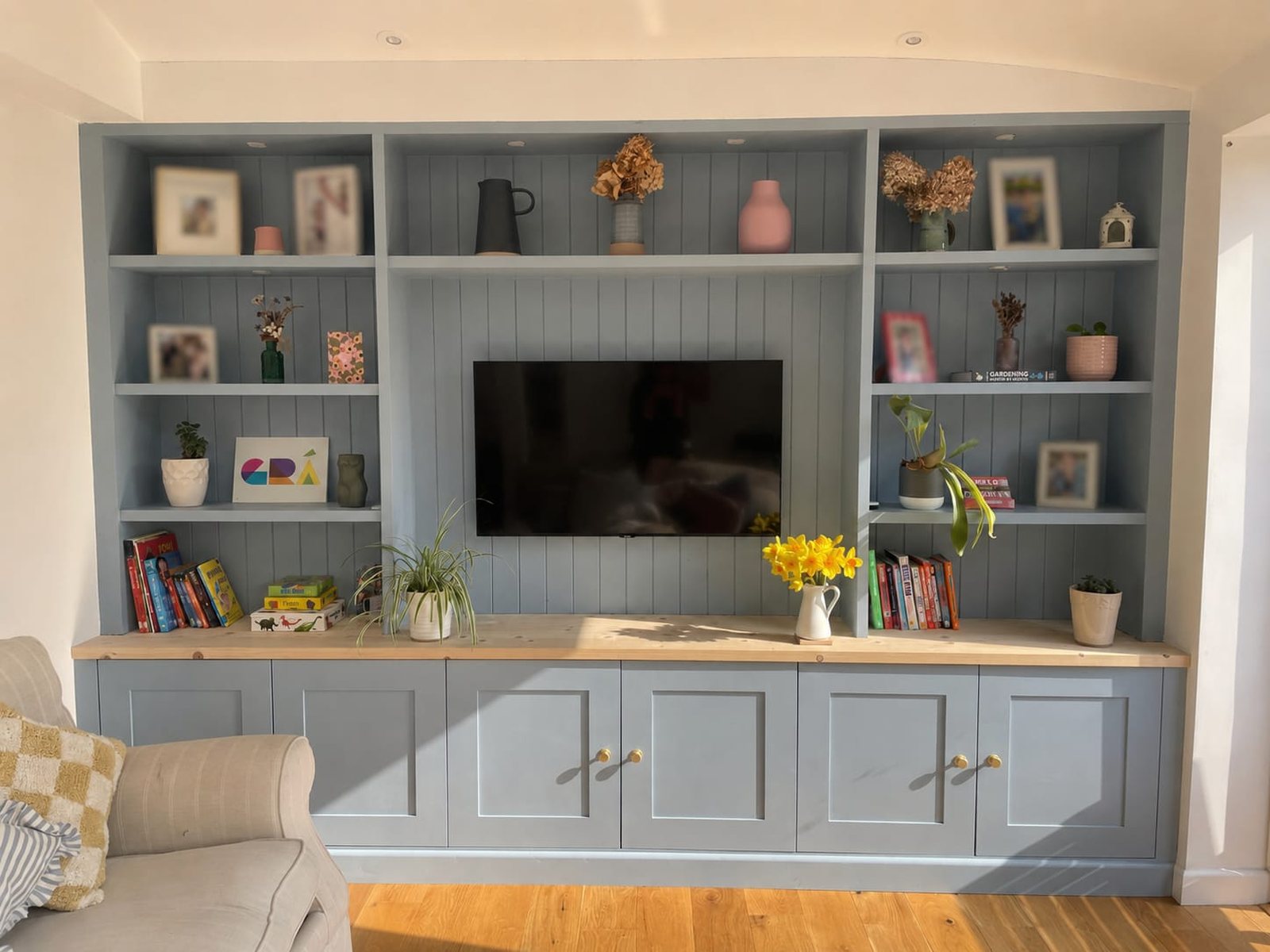 A finished media wall in soft blue-grey with open shelving, TV and base cupboards in a sunny living room